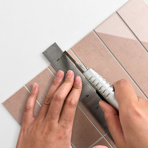 Pastellrosa Klebefliesen mit Cuttermesser und Lineal zuschneiden